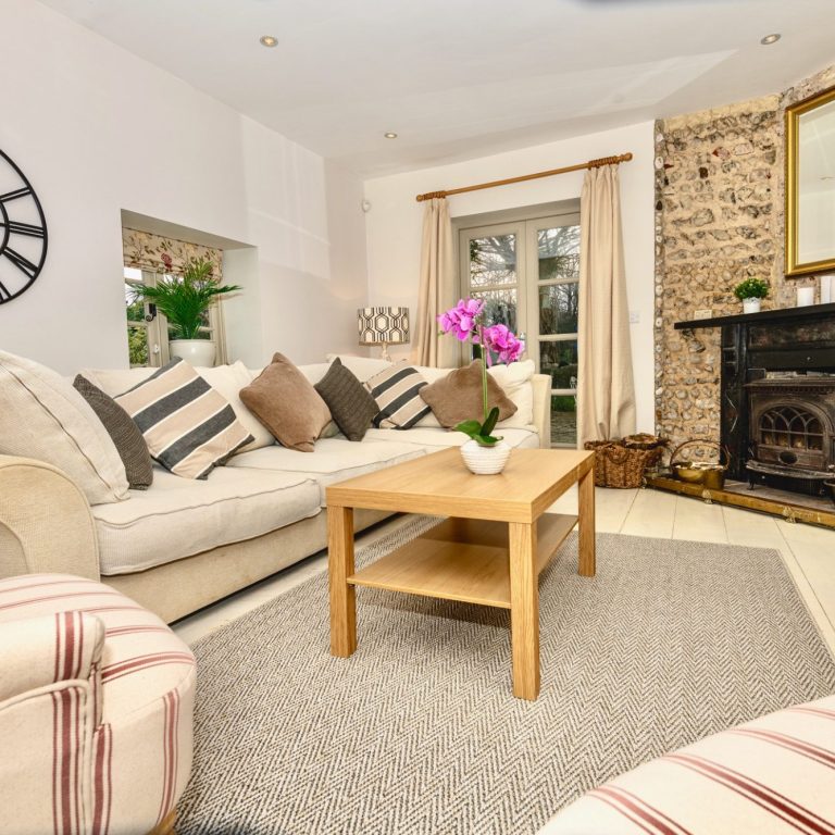A cosy living room in with a sofa, coffee table, and floral decor by a fireplace.