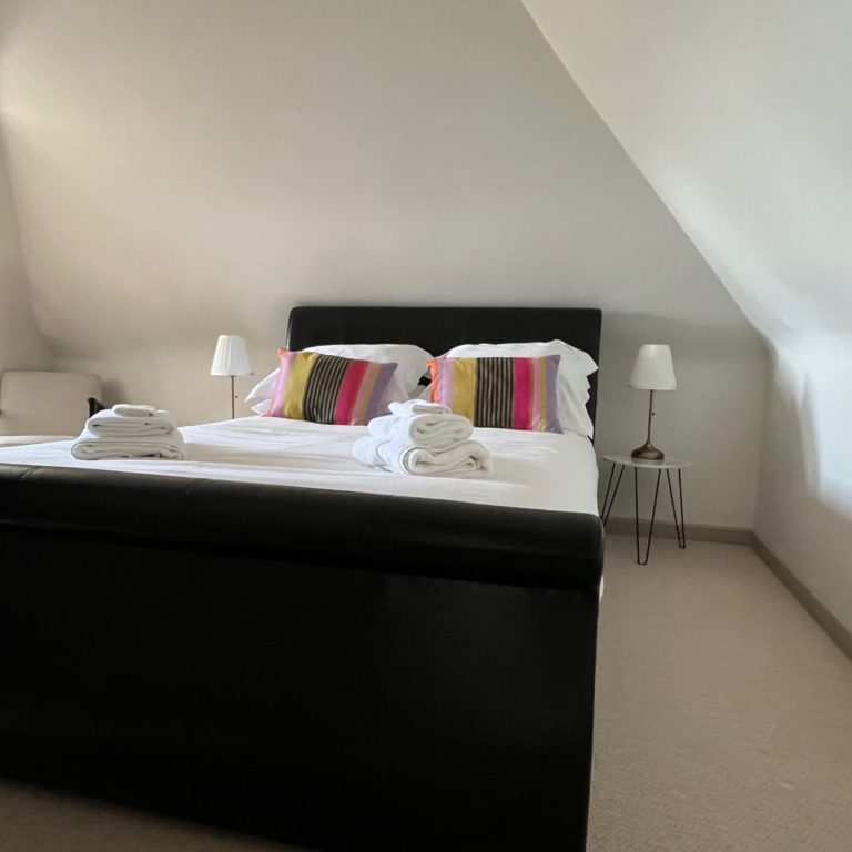 Bedroom with a double bed, colourful cushions, and bedside lamps in a modern setting.
