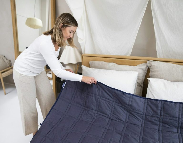 Woman arranging a navy blue bedspread on a neatly made bed with pillows.